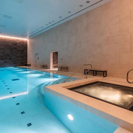 Citysuites 2 Aparthotel マンチェスター エクステリア 写真 The photo shows an indoor swimming pool area. The pool is a bright blue color and features smooth, tiled surfaces. On one side, there is a hot tub area with steps leading into it. The walls are made of light-colored stone, and there is ambient lighti
