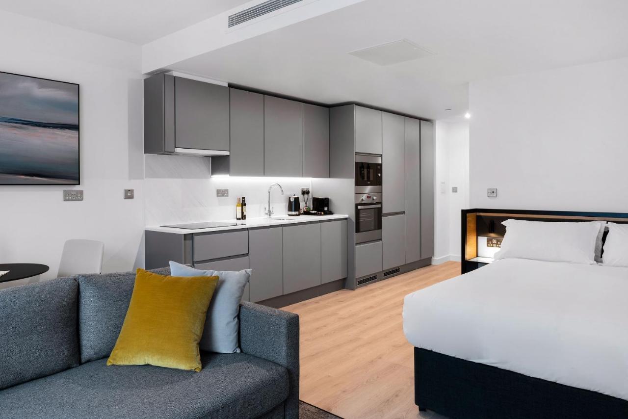 Citysuites 2 Aparthotel マンチェスター エクステリア 写真 The photo shows a modern studio apartment featuring an open-plan layout. On one side, there is a kitchenette with sleek, gray cabinets and appliances, including a coffee maker and oven. Adjacent to the kitchenette is a small dining area with a table 