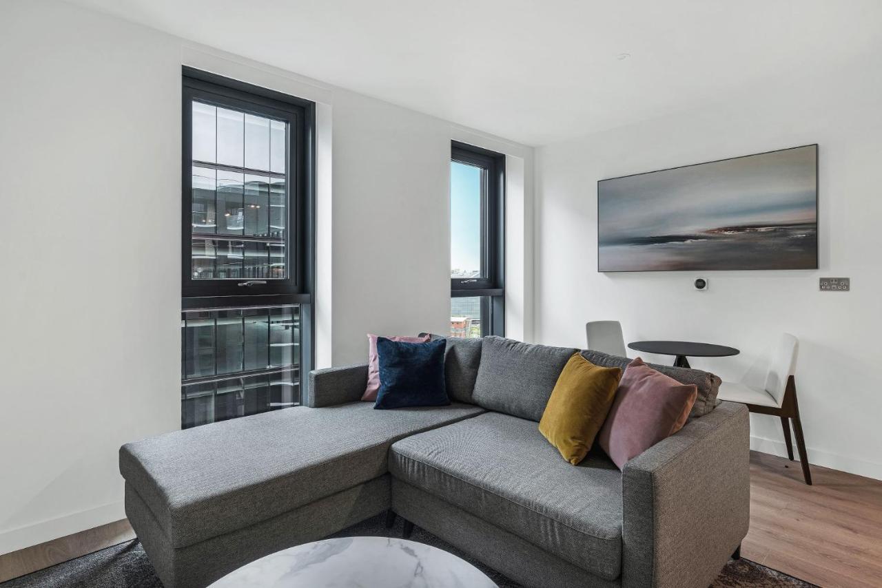 Citysuites 2 Aparthotel マンチェスター エクステリア 写真 The photo shows a modern living space featuring a gray sectional sofa adorned with colorful throw pillows. There are large windows allowing natural light to fill the room, offering a view of the outdoors. A wall-mounted television is positioned above