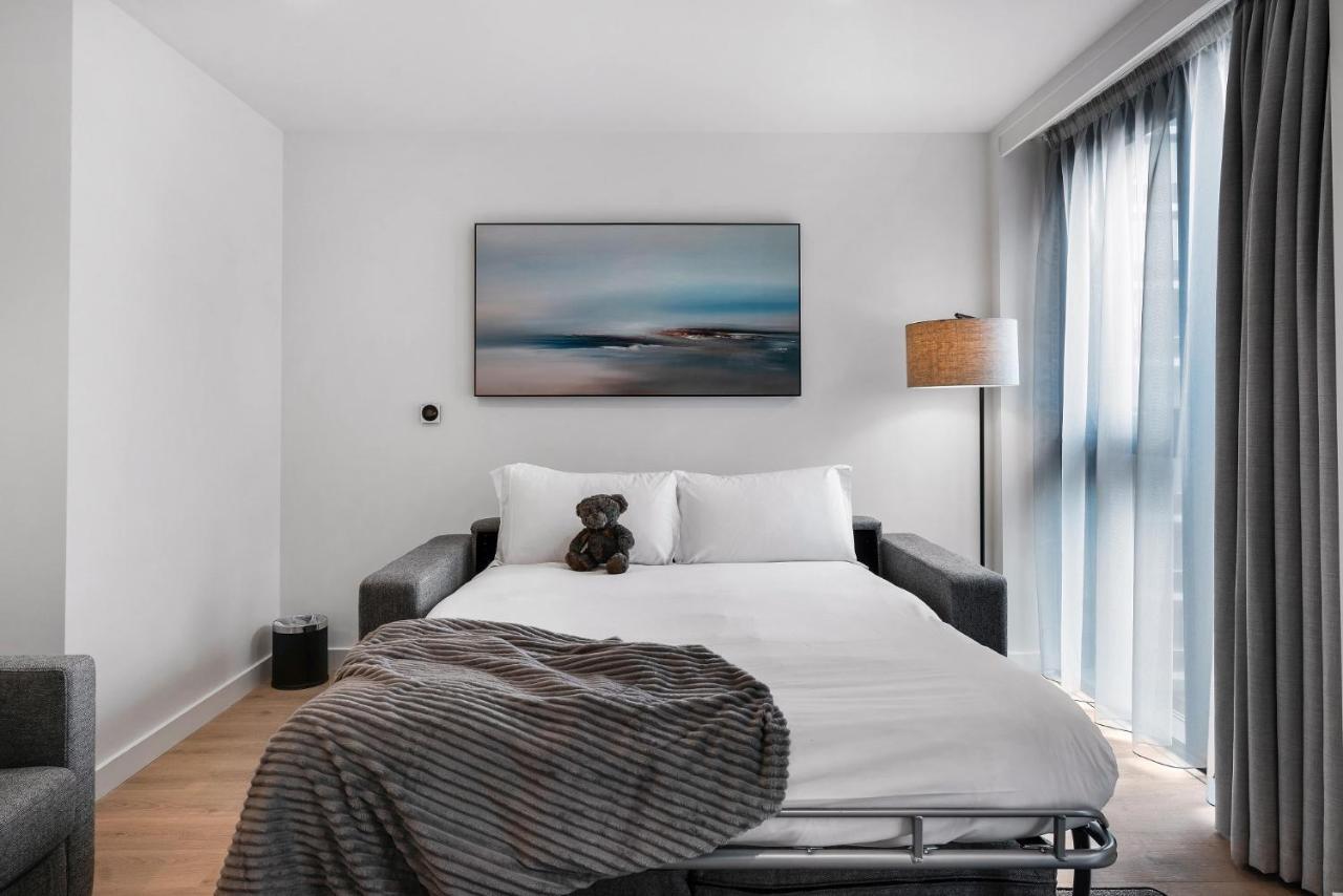 Citysuites 2 Aparthotel マンチェスター エクステリア 写真 The photo shows a modern bedroom featuring a bed with white bedding and a decorative throw blanket. There is a teddy bear placed on the bed. A piece of abstract art is hanging on the wall above the bed. The room has a large window with sheer curtains
