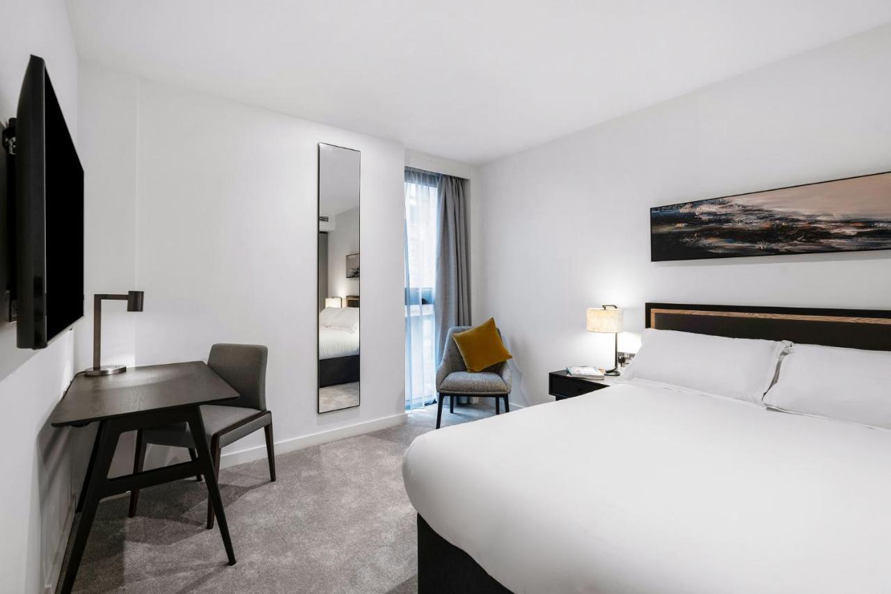Citysuites 2 Aparthotel マンチェスター エクステリア 写真 The photo shows a modern hotel room with a clean and minimalist design. It features a large bed with white linens, a small desk with a chair, and a mirror mounted on the wall. There is a chair in one corner with a decorative pillow, and the room has 