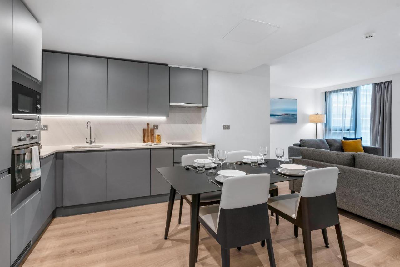 Citysuites 2 Aparthotel マンチェスター エクステリア 写真 The photo shows a modern, open-concept kitchen and living area. The kitchen features sleek, gray cabinetry with a countertop, a sink, and built-in appliances. There are cooking utensils displayed on the countertop. Next to the kitchen, there is a din