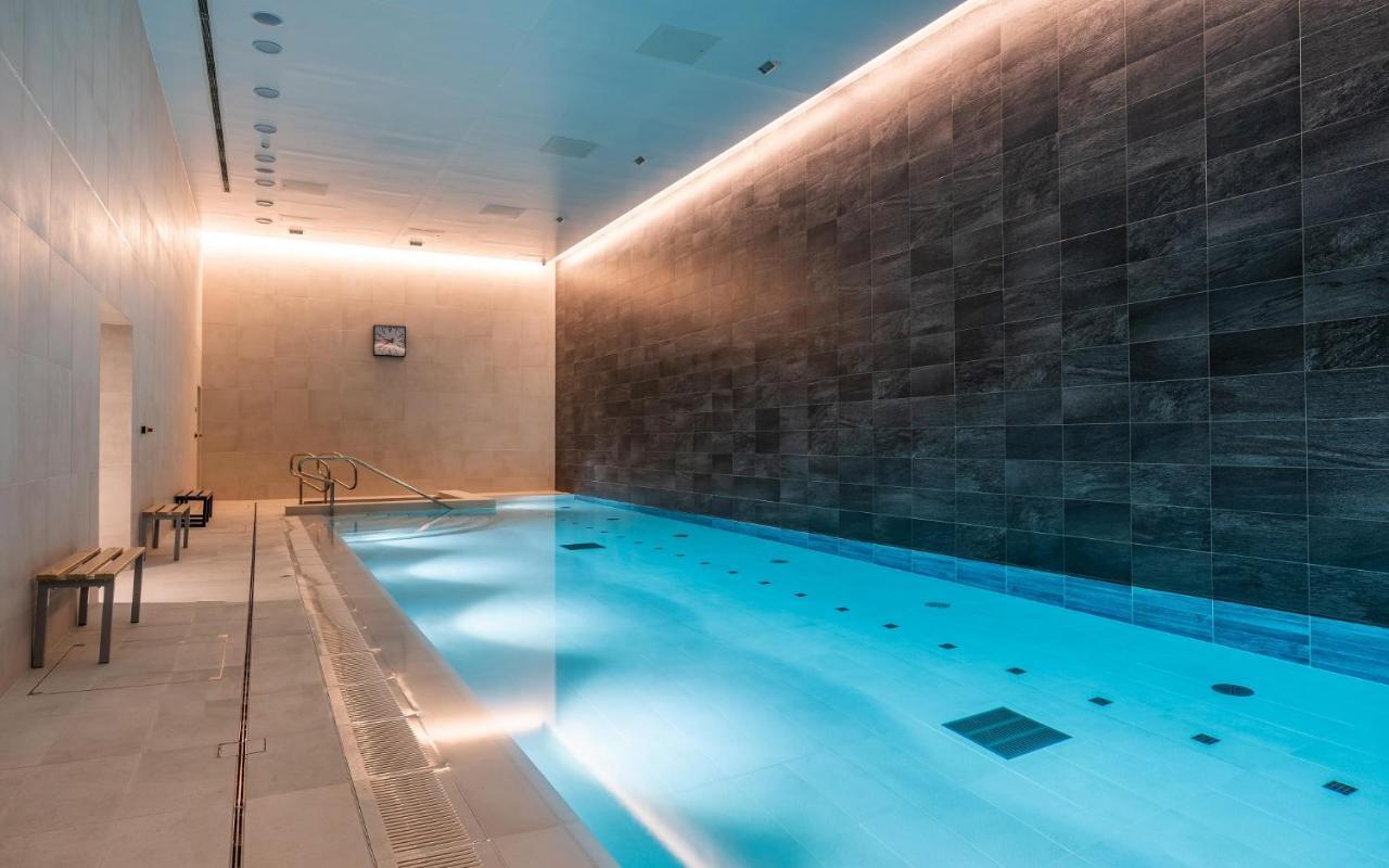 Citysuites 2 Aparthotel マンチェスター エクステリア 写真 The photo shows an indoor swimming pool area. The pool is illuminated with a soft blue light, creating a calming atmosphere. The walls are designed with dark tiles, and there is a lighter tiled area surrounding the pool. Ambient lighting is installed