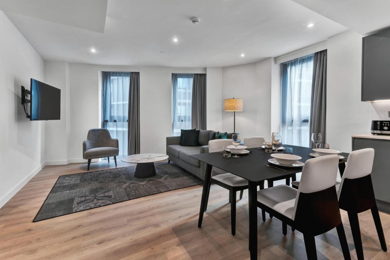 Citysuites 2 Aparthotel マンチェスター エクステリア 写真 The photo shows a modern living space that includes a living area and dining area. 

- **Living Area**: There's a gray sofa with a coffee table in front of it, along with a single armchair. A large flat-screen TV is mounted on the wall. The space is 