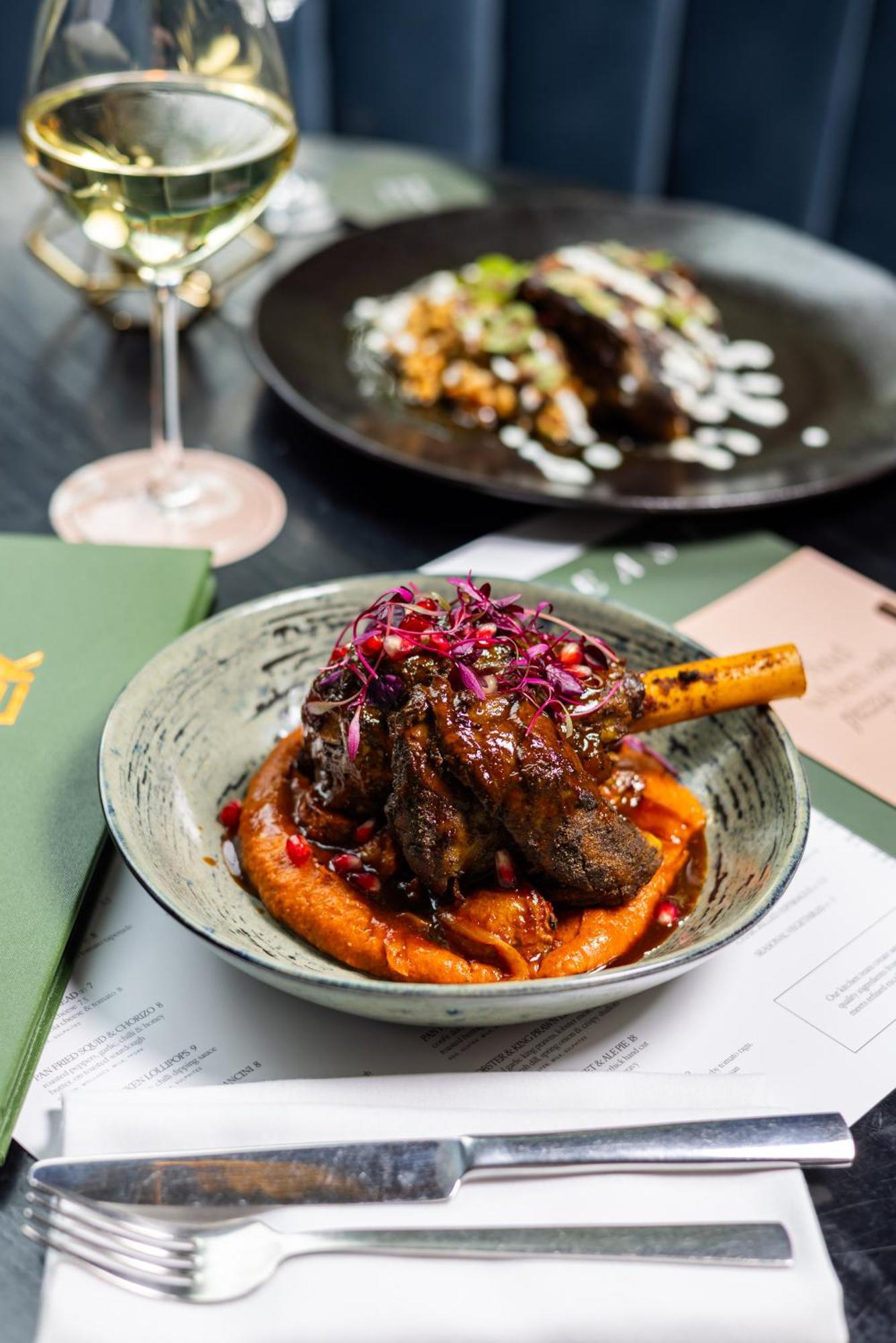Citysuites 2 Aparthotel マンチェスター エクステリア 写真 The photo showcases a beautifully presented dish featuring a piece of slow-cooked meat with a bone, likely lamb, sitting atop a vibrant orange puree. The meat is glazed with a rich sauce and garnished with small pieces of red pomegranate and purple m