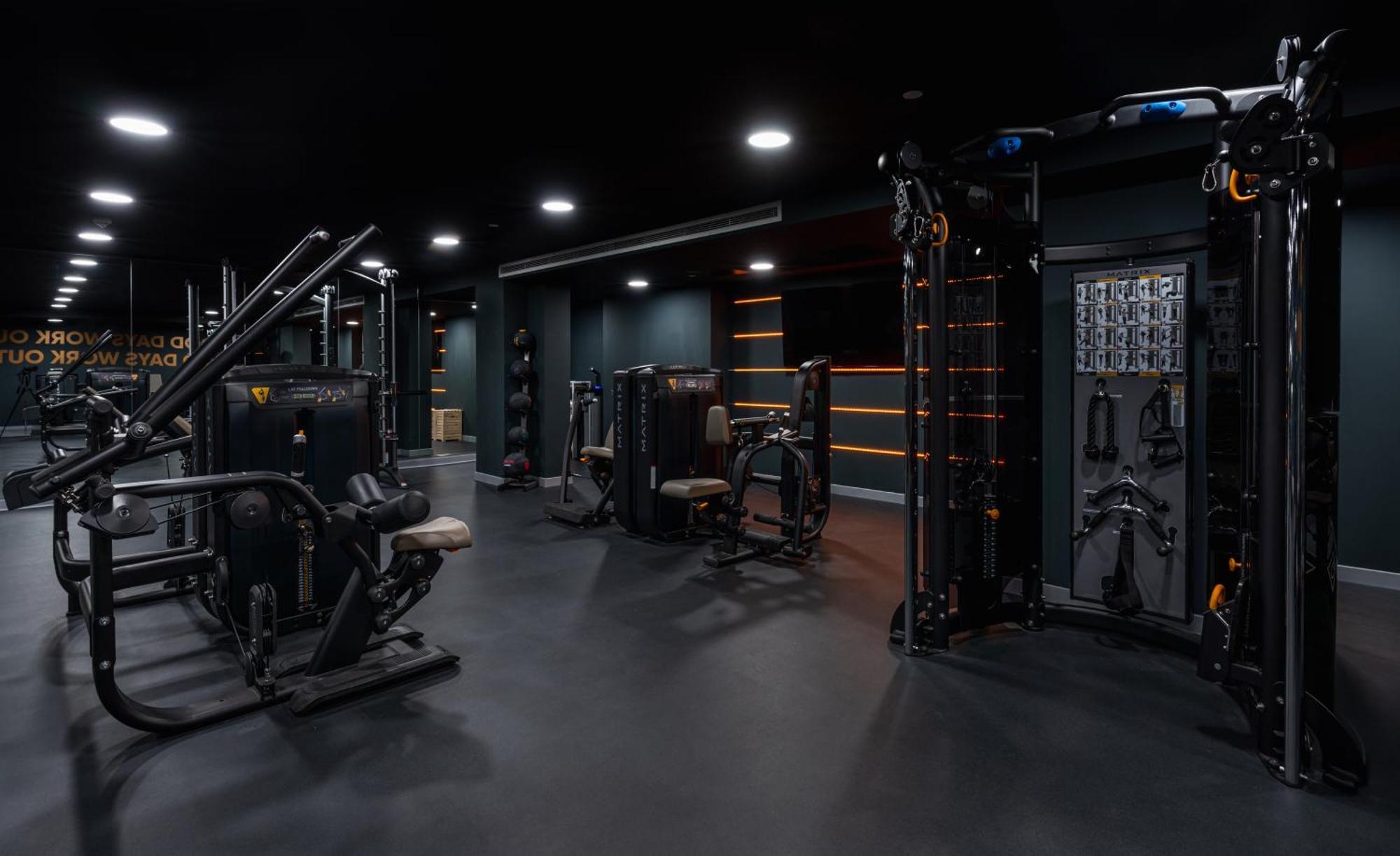 Citysuites 2 Aparthotel マンチェスター エクステリア 写真 The photo shows a modern gym or fitness area with various workout machines. The space has a dark color scheme, featuring black walls and flooring. There are multiple pieces of exercise equipment, including stations for strength training, possibly tar