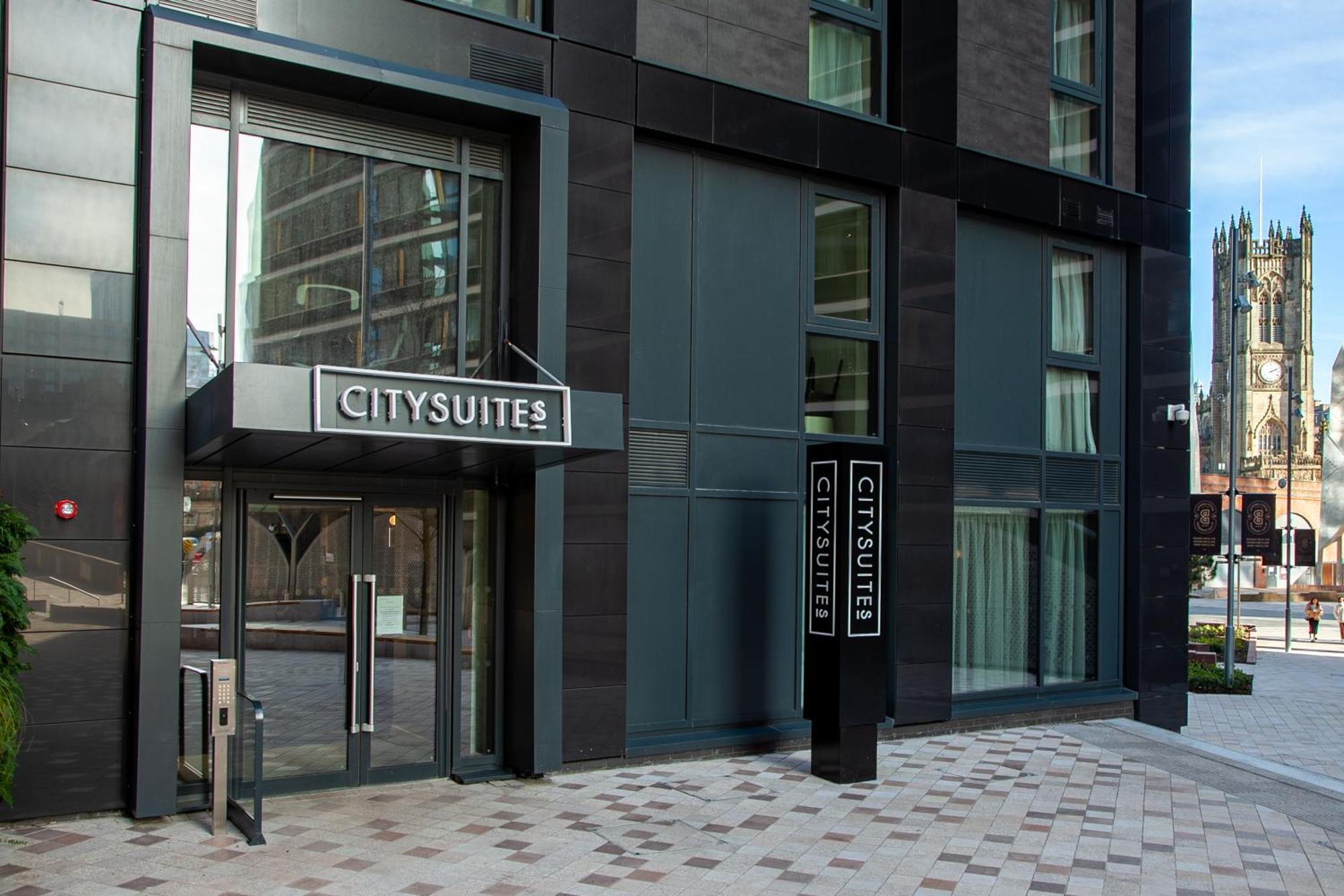 Citysuites 2 Aparthotel マンチェスター エクステリア 写真 The photo shows the entrance to a modern building labeled "CITYSUITES." The entrance features large glass doors and a sleek, contemporary design. The building has dark exterior panels and large windows, suggesting a stylish and urban environment. The