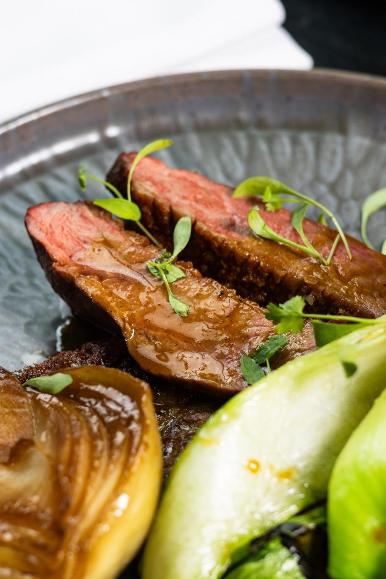 Citysuites 2 Aparthotel マンチェスター エクステリア 写真 The photo features slices of meat, likely beef, presented on a decorative plate. The meat appears to have a rich brown sauce drizzled over it and is garnished with fresh herbs, adding a pop of green. There are also some slices of a light-colored vege