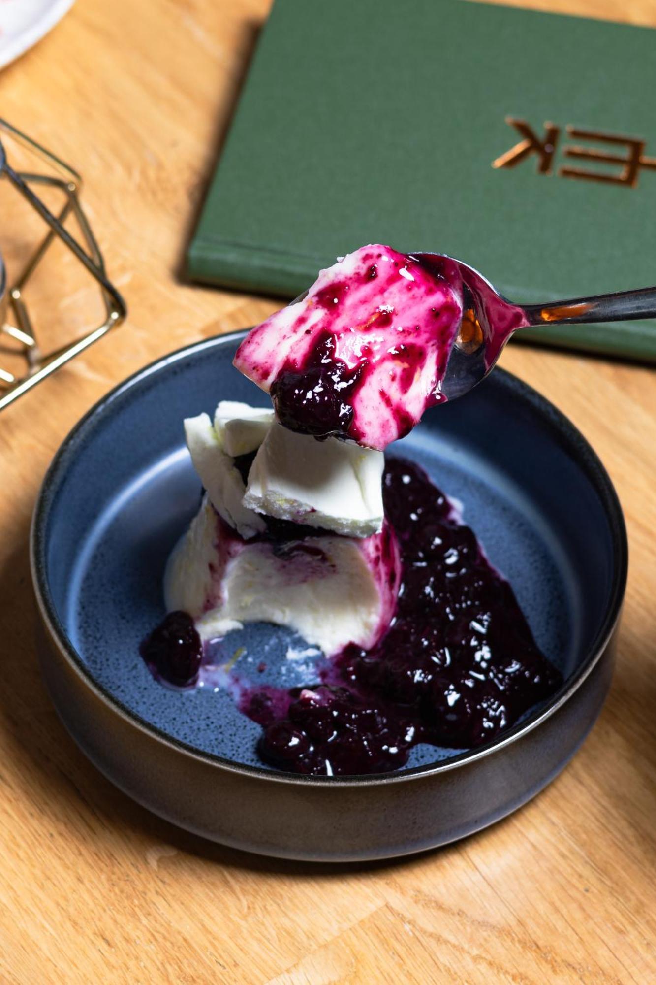 Citysuites 2 Aparthotel マンチェスター エクステリア 写真 The photo shows a serving of dessert, likely a type of panna cotta or a creamy custard, partially dished out and accompanied by a rich berry sauce, possibly made from blueberries or blackberries. A spoon with some of the dessert and sauce is hovering